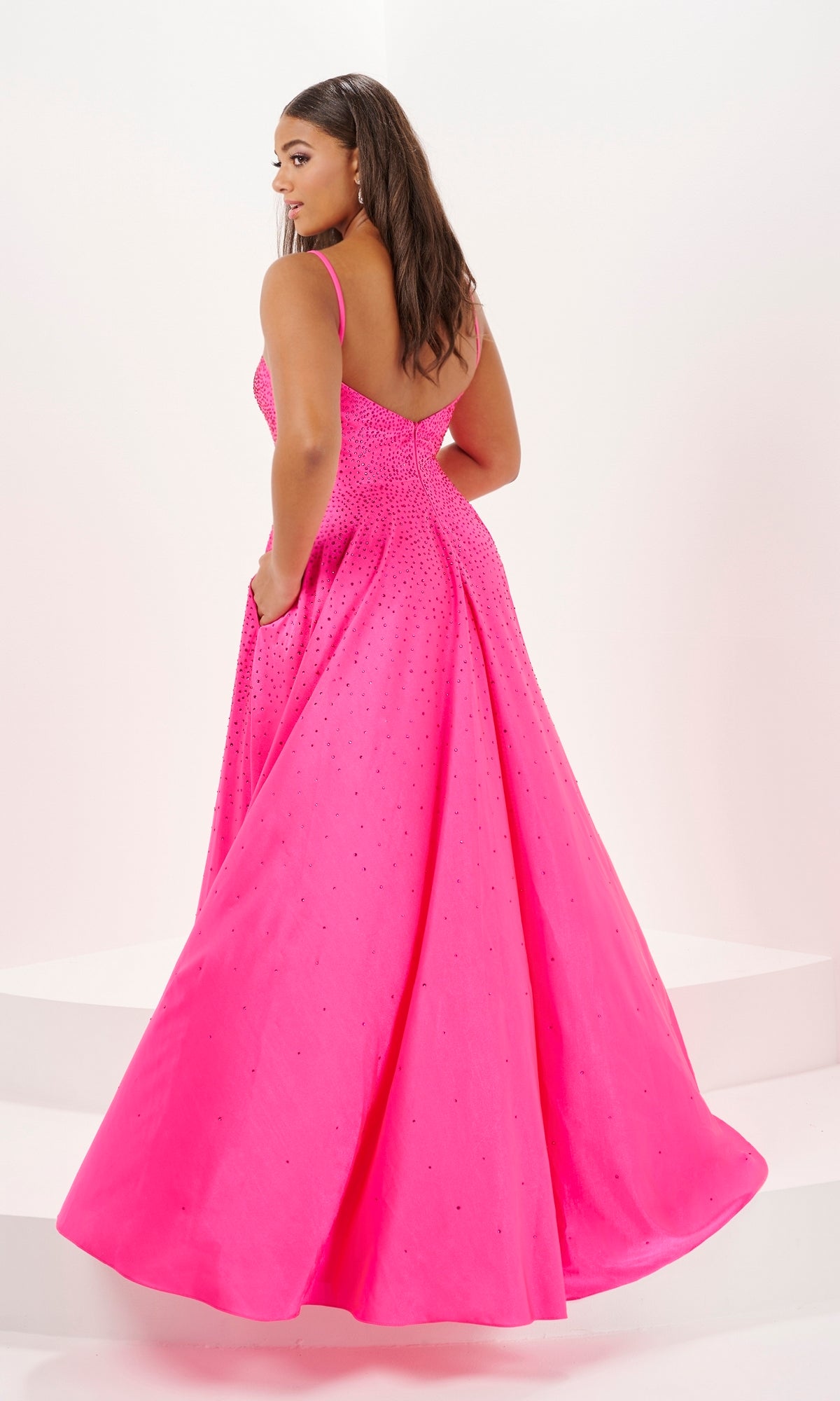 Woman in a sage green, floor-length Tiffany Plus-Size A-Line Prom Dress 16122 with thin straps and rhinestone embellishments, standing on white steps and looking over her shoulder.